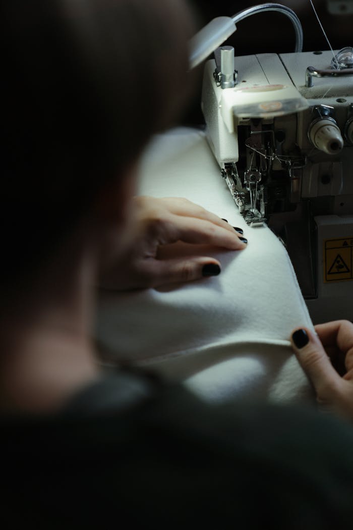 Focused seamstress using sewing machine for fabric stitching indoors.